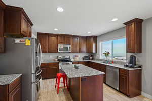 Kitchen with stainless steel appliances, light wood-style flooring, recessed lighting, a kitchen breakfast bar, and light stone counters