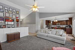 Living room featuring lofted ceiling, a chandelier, a wainscoted wall, ceiling fan, and a decorative wall