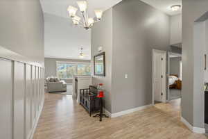 Hallway with high vaulted ceiling, light wood-type flooring, an upstairs landing, and a chandelier