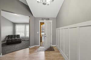Entrance foyer with vaulted ceiling, light wood finished floors, and a chandelier