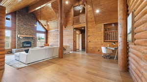 Living area featuring rustic walls, high vaulted ceiling, a wooden ceiling with exposed beams, a fireplace, and wood-type flooring