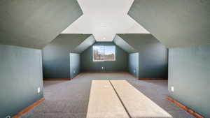 Bonus room featuring lofted ceiling, carpet flooring, and a textured wall