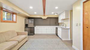 Downstairs mother in law family room and kitchen with seperate garage entrance. Featuring white cabinets, light countertops, appliances with stainless steel finishes, beamed ceiling, and recessed lighting
