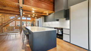 Kitchen with light countertops, rustic walls, a kitchen island, light wood-style flooring, and a wooden ceiling with exposed beams