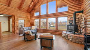 Living area with high vaulted ceiling, a wood stove, hardwood / wood-style flooring, a wood ceiling with exposed beams, and log walls