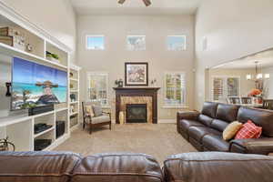 Carpeted living area with a towering ceiling, a fireplace, a chandelier, ceiling fan, and built in shelves