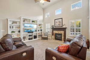 Living area with high vaulted ceiling, a high end fireplace, a ceiling fan, and carpet floors