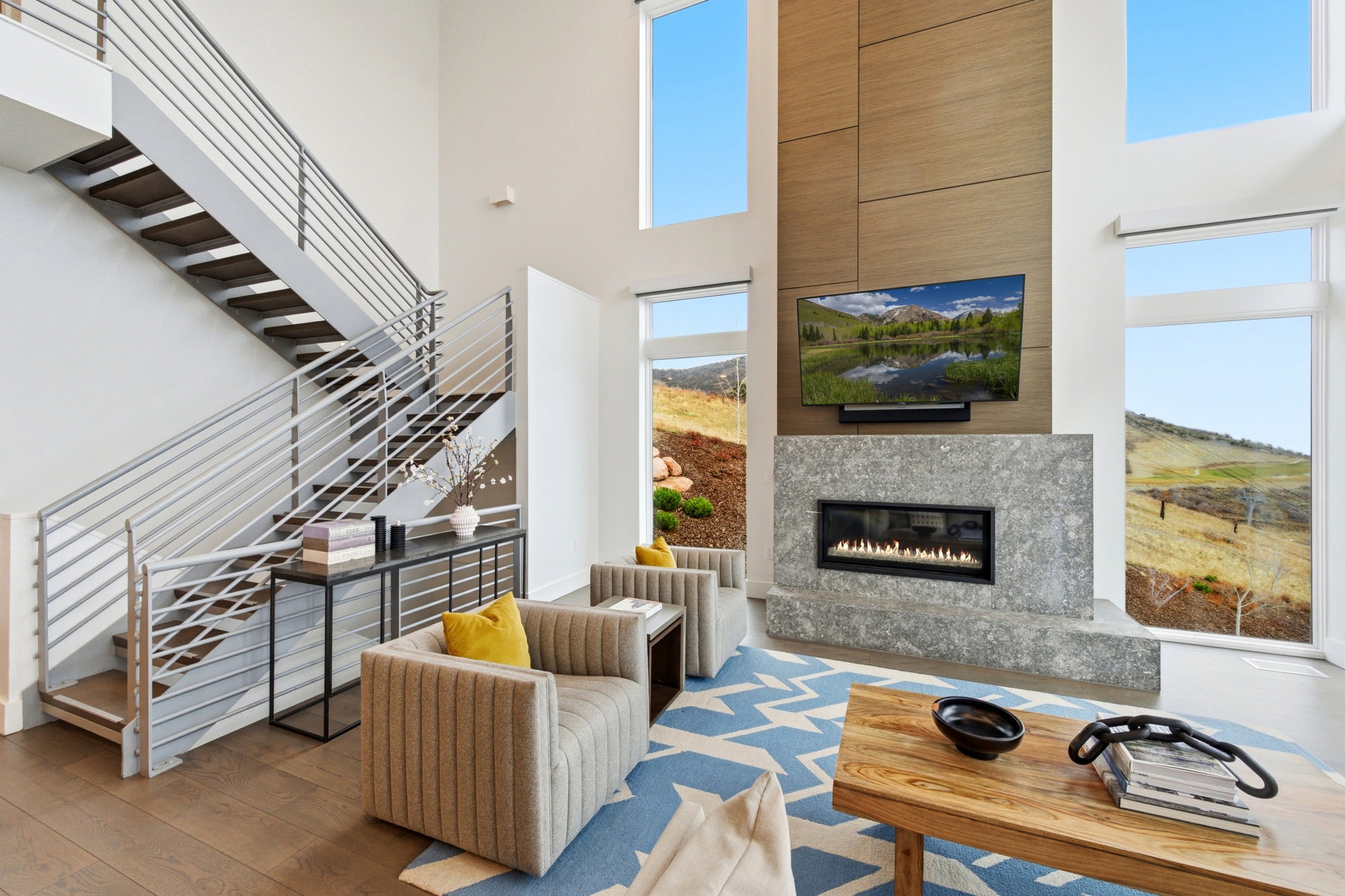 Living area with a towering ceiling, a glass covered fireplace, wood-type flooring, and stairs