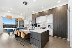 Kitchen with dark brown cabinets, white cabinets, modern cabinets, hanging light fixtures, and a center island with sink