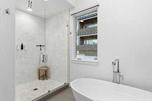Bathroom featuring a freestanding bath, a marble finish shower, and tile patterned flooring