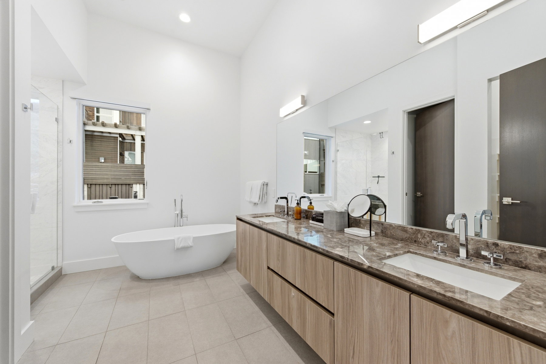 Full bath with double vanity, a stall shower, light tile patterned flooring, a freestanding tub, and recessed lighting