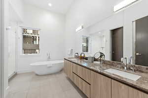 Full bath with double vanity, a stall shower, light tile patterned flooring, a freestanding tub, and recessed lighting