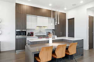 Kitchen featuring modern cabinets, white cabinetry, a center island with sink, a breakfast bar area, and dark brown cabinetry