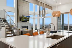 Kitchen featuring modern cabinets, dark brown cabinetry, a glass covered fireplace, decorative light fixtures, and a towering ceiling