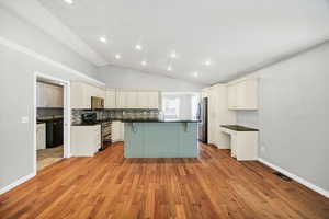 Kitchen with a kitchen breakfast bar, appliances with stainless steel finishes, vaulted ceiling, light wood-type flooring, and a kitchen island with sink