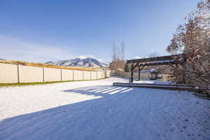 Yard layered in snow with a fenced backyard, a deck with mountain view, and a pergola