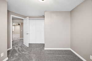 Unfurnished bedroom with dark colored carpet, a closet, arched walkways, and a textured ceiling
