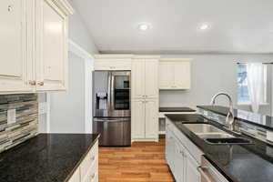 Kitchen featuring stainless steel appliances, light wood finished floors, recessed lighting, dark stone countertops, and tasteful backsplash