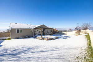 Snow covered house with a fenced backyard, a deck, and a pergola