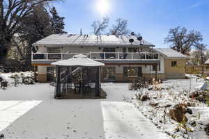 Snow covered rear of property featuring brick siding, a chimney, a balcony, and a wooden deck