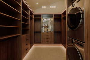 Spacious closet with lofted ceiling, stacked washing machine and dryer, and light colored carpet