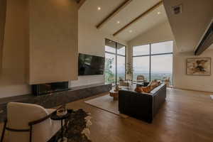 Living room with a premium fireplace, beamed ceiling, hardwood / wood-style flooring, high vaulted ceiling, and recessed lighting