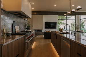 Kitchen featuring modern cabinets, dark stone countertops, appliances with stainless steel finishes, backsplash, and light wood-type flooring