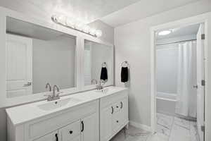 Full bath featuring light marble finish floors, double vanity, and shower / bathtub combination with curtain