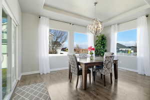 Dining space with a tray ceiling, healthy amount of natural light, light wood-style floors, and a chandelier