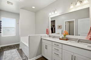 Full bathroom featuring double vanity, a garden tub, dark wood-type flooring, and recessed lighting
