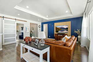 Living area featuring a barn door, a raised ceiling, wood finished floors, and recessed lighting