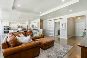 Living room featuring a barn door, a chandelier, wood finished floors, recessed lighting, and a tray ceiling