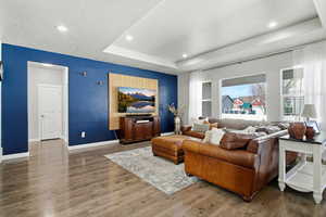 Living room with a tray ceiling, wood finished floors, and recessed lighting
