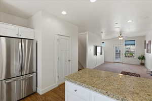 Kitchen featuring white cabinets, freestanding refrigerator, open floor plan, light stone counters, and recessed lighting