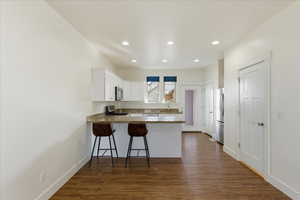 Kitchen featuring white cabinetry, dark wood-type flooring, a peninsula, dark stone counters, and stainless steel appliances