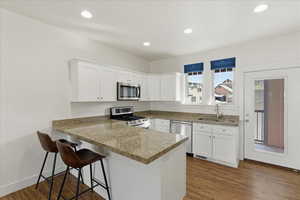 Kitchen with white cabinets, a peninsula, stainless steel appliances, a kitchen breakfast bar, and dark wood finished floors