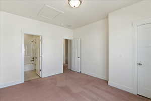Unfurnished bedroom featuring light colored carpet, ensuite bath, and attic access