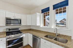 Kitchen with stainless steel appliances, white cabinets, light stone countertops, and dark wood-style flooring