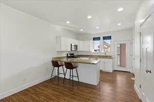 Kitchen featuring white cabinetry, appliances with stainless steel finishes, a peninsula, a kitchen breakfast bar, and dark wood-style floors