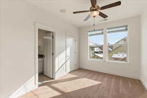 Unfurnished bedroom with ceiling fan, light colored carpet, and ensuite bath