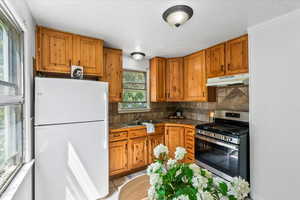 Kitchen with freestanding refrigerator, stainless steel gas range oven, brown cabinetry, and under cabinet range hood
