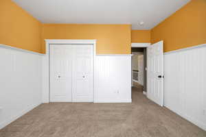 Unfurnished bedroom with a wainscoted wall, carpet flooring, and a closet