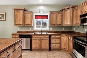 Kitchen featuring stainless steel appliances, dark countertops, brown cabinets, and light tile patterned floors