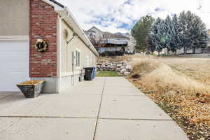 View of side of home with brick siding, a garage, stucco siding, and a patio