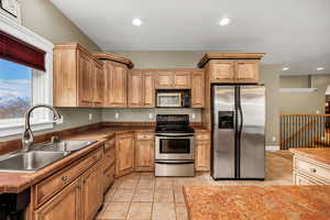 Kitchen featuring stainless steel appliances, light tile patterned floors, recessed lighting, brown cabinets, and dark countertops