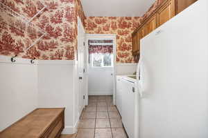Laundry area with wallpapered walls, wainscoting, cabinet space, separate washer and dryer, and light tile patterned flooring