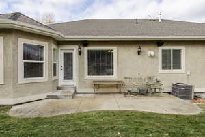 View of exterior entry featuring stucco siding, a patio area, a shingled roof, and a yard