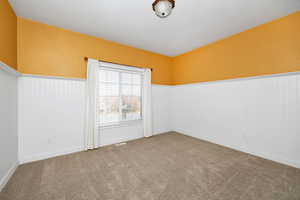 Empty room featuring a wainscoted wall and carpet flooring