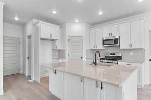 Kitchen featuring white cabinetry, stainless steel appliances, tasteful backsplash, light stone countertops, and light wood-style flooring