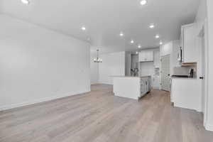 Kitchen with backsplash, an island with sink, white cabinets, a chandelier, and recessed lighting